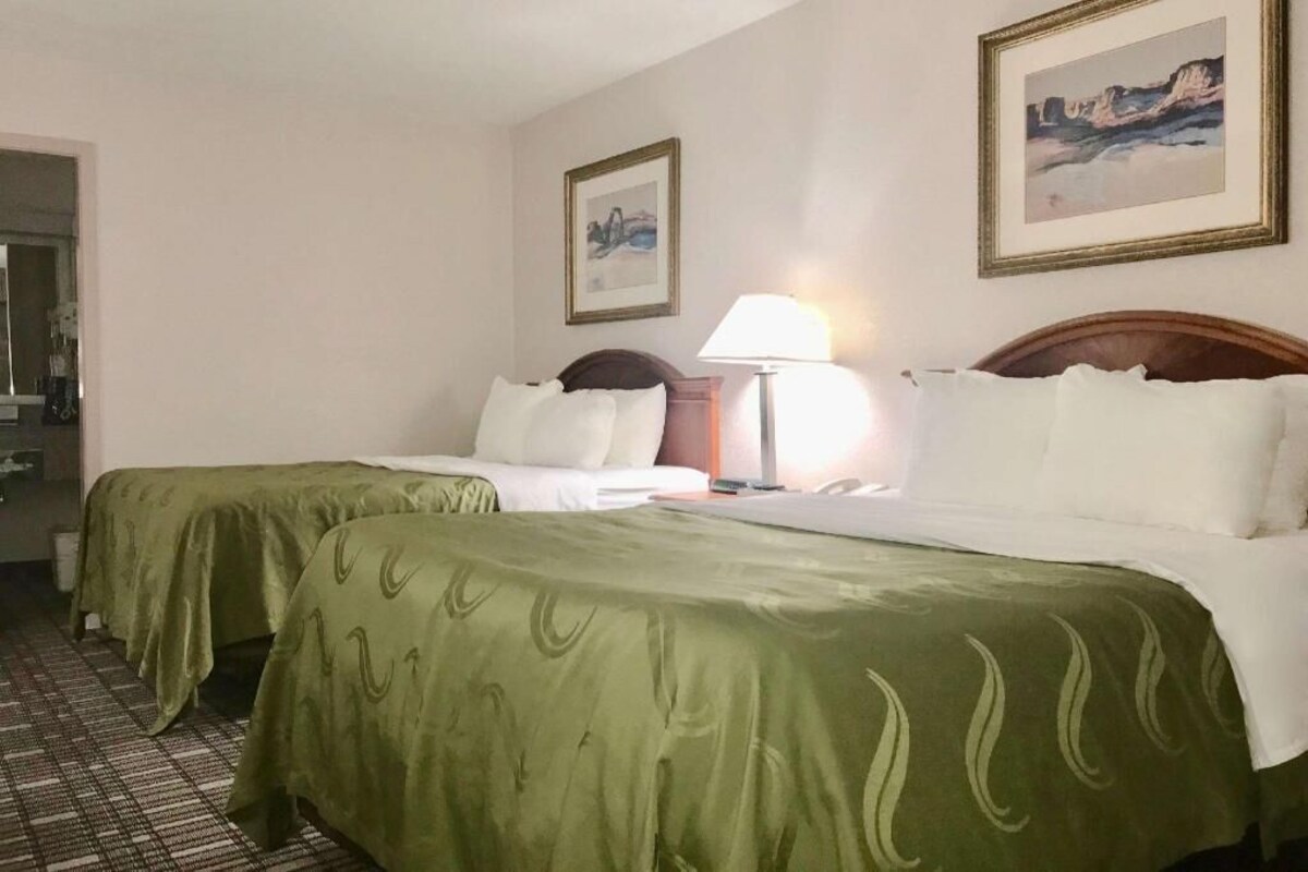 A hotel room with two beds, a nightstand, a lamp, and framed artwork on the walls.