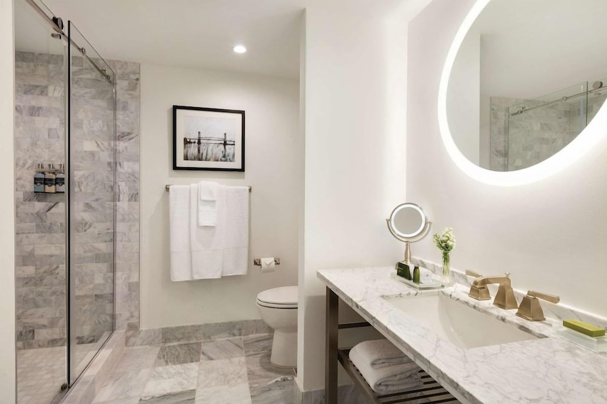 Un baño con cabina de ducha de vidrio, inodoro, lavabo con tocador y un cuadro en la pared.