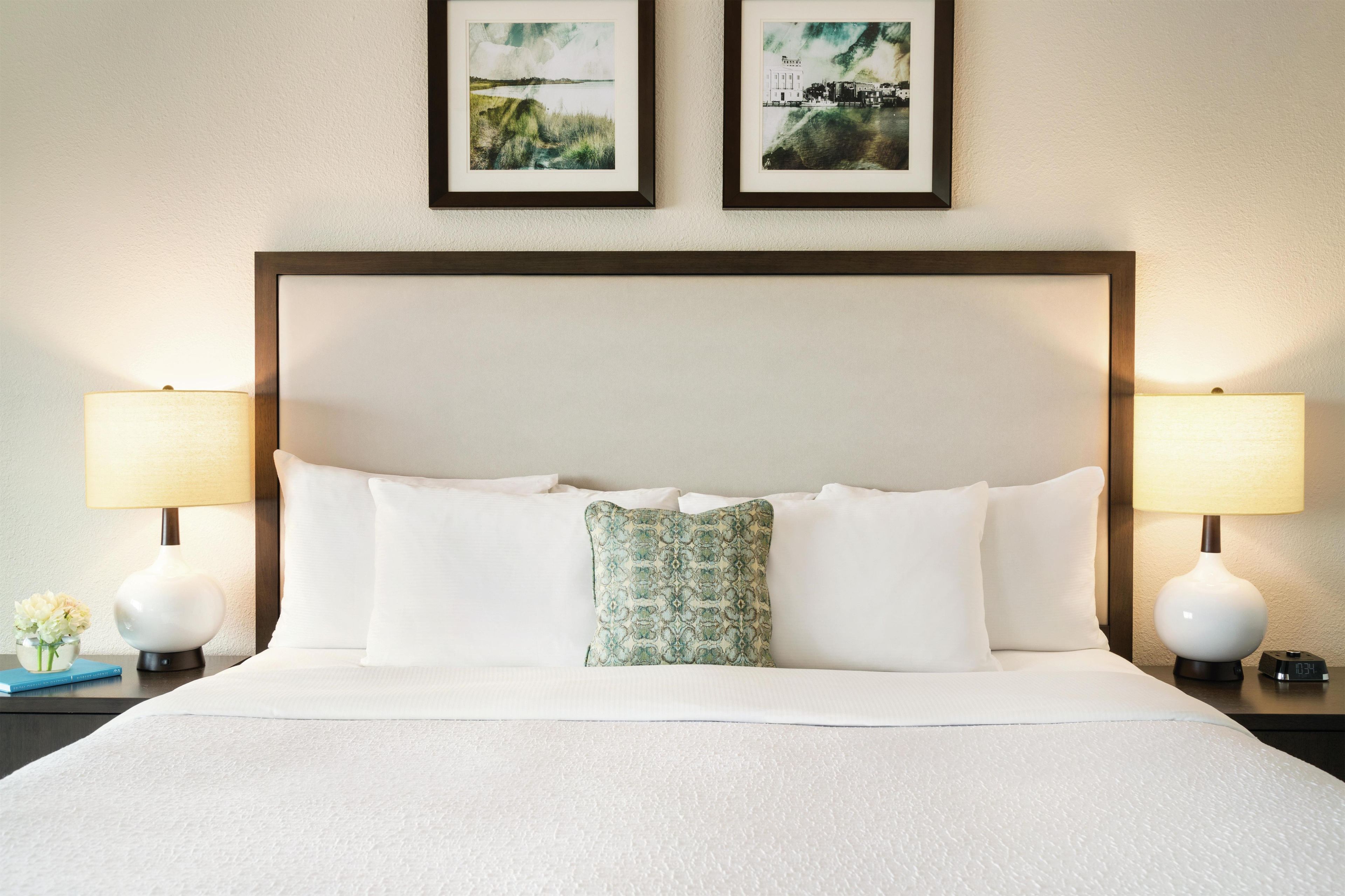 Ein Hotelzimmer mit einem großen Bett, zwei Nachttischlampen und zwei gerahmten Bildern an der Wand.