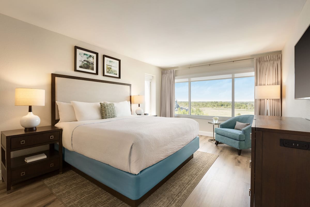 A hotel room with a large bed, a desk, a chair, and a view of the outdoors.