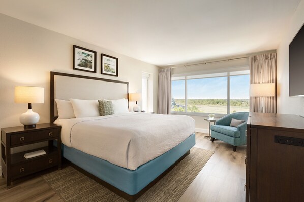 Habitación de hotel con una cama grande, un escritorio, una silla y vistas al exterior.