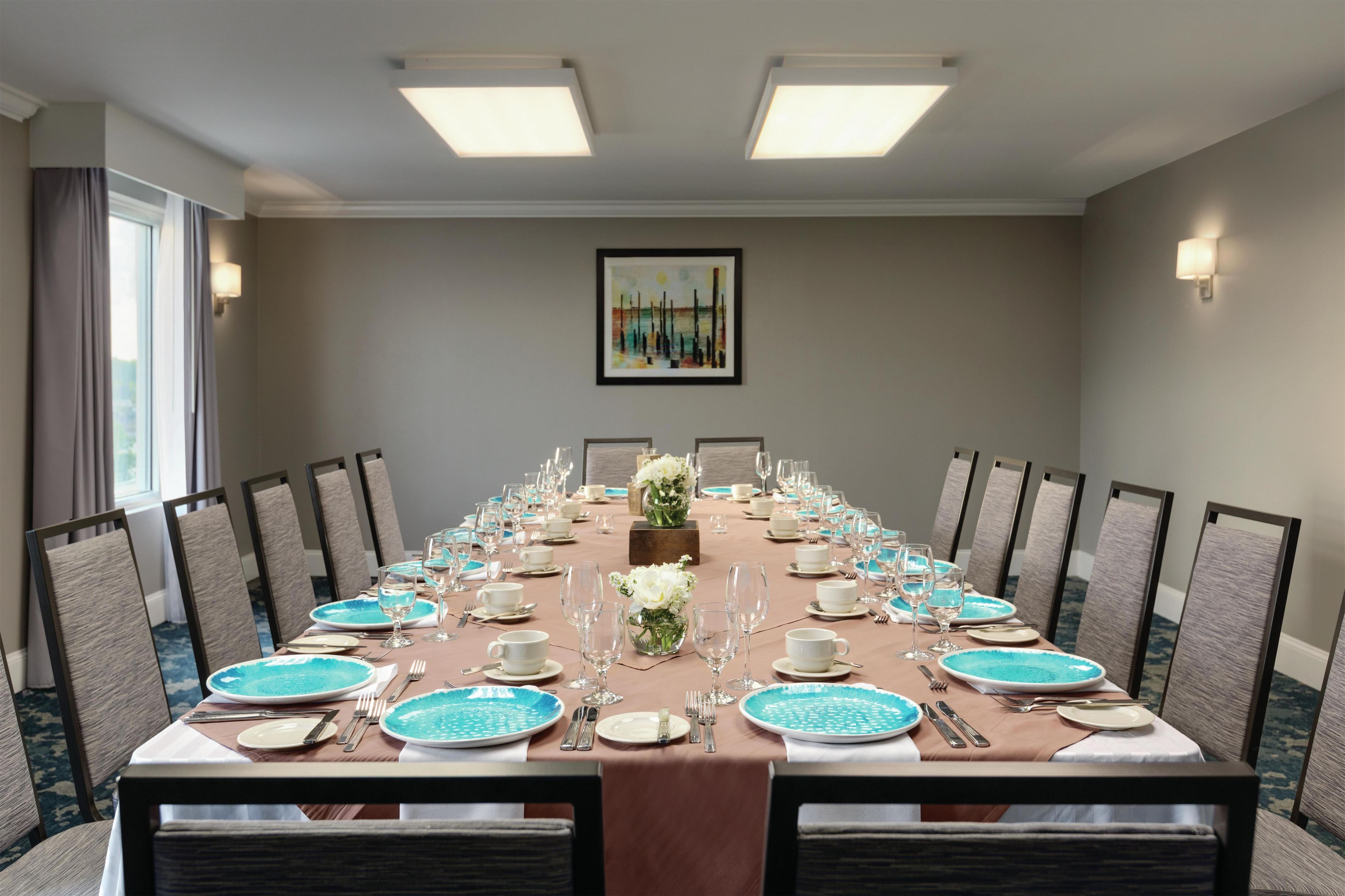 A conference room with a long table set for a meeting, equipped with chairs, plates, glasses, and cutlery.