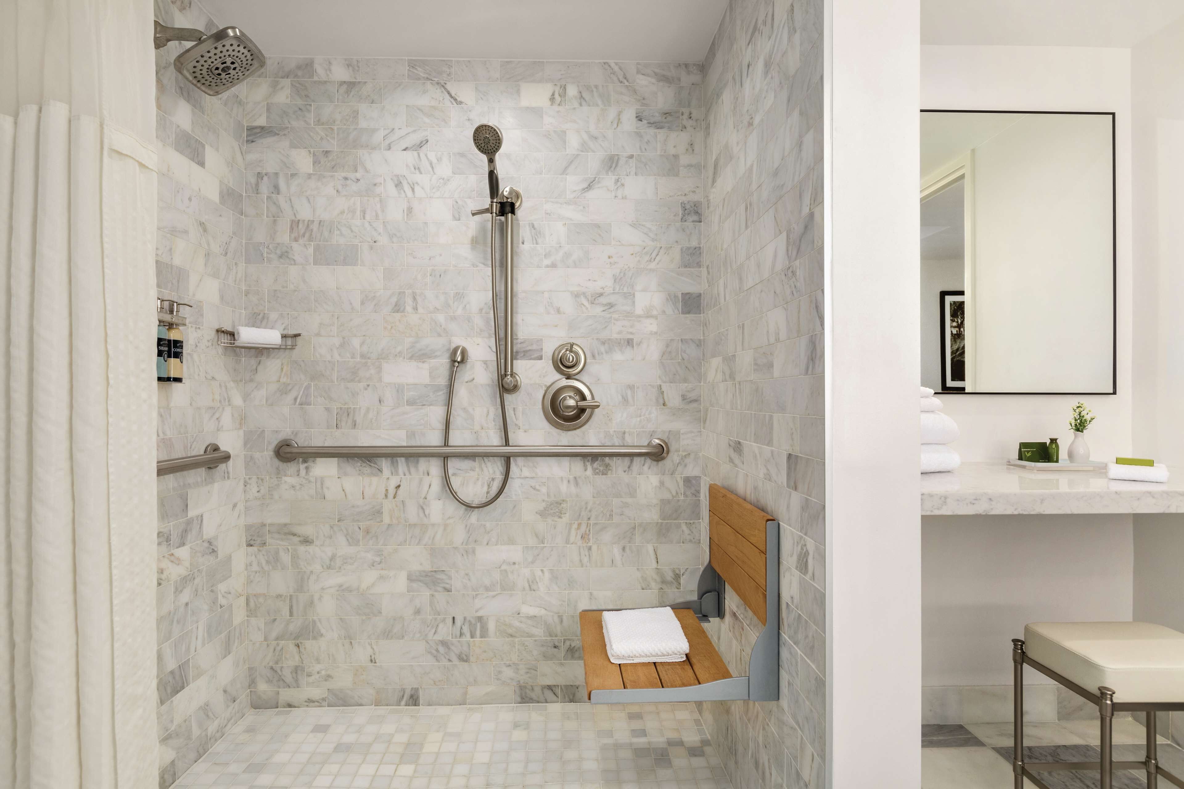 A modern bathroom with a shower, a bench, and a vanity area.