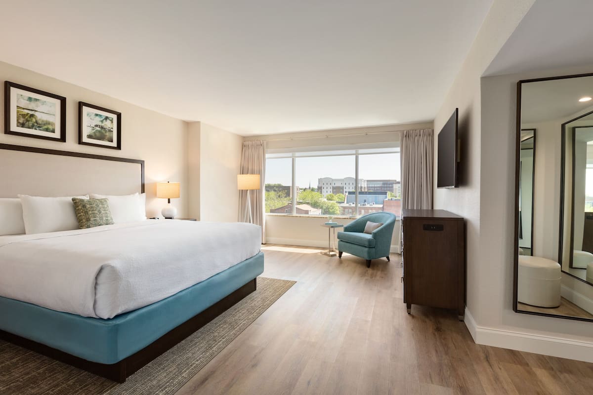 A hotel room with a large bed, a desk, a chair, and a TV.