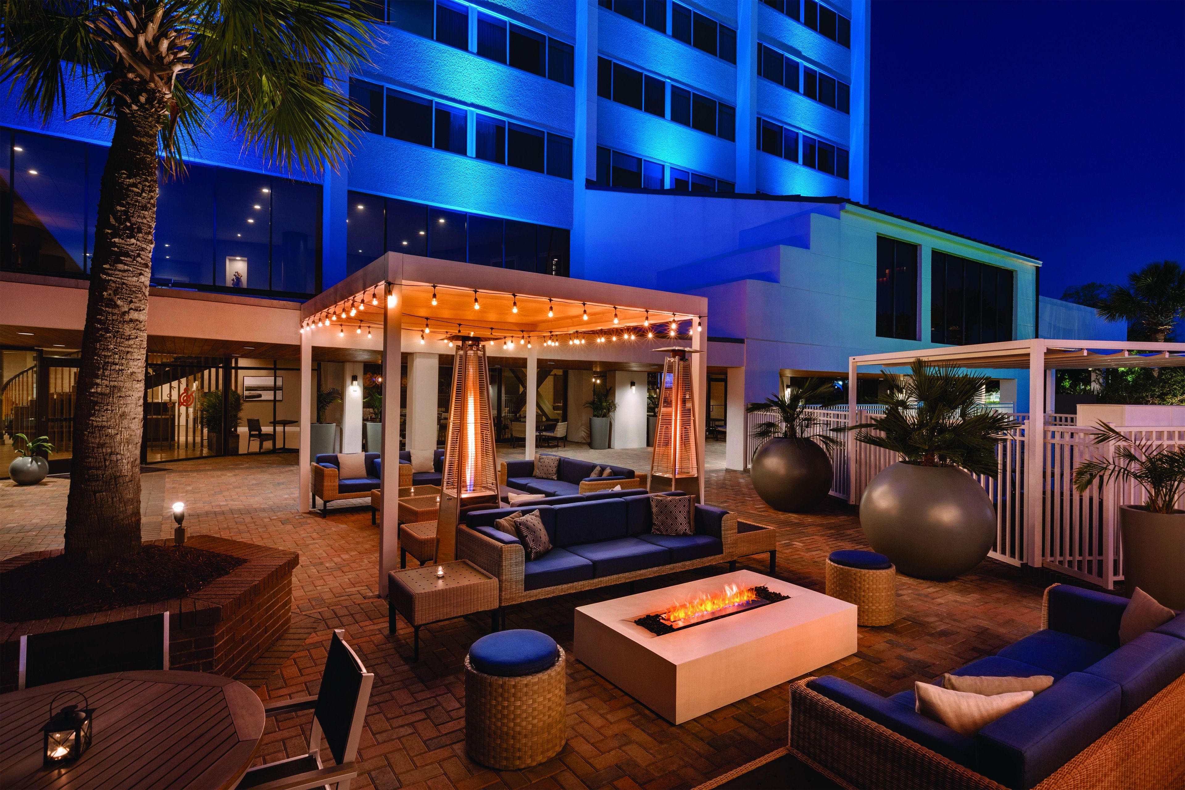 An outdoor lounge area with seating, a fire feature, and a covered seating area with string lights.