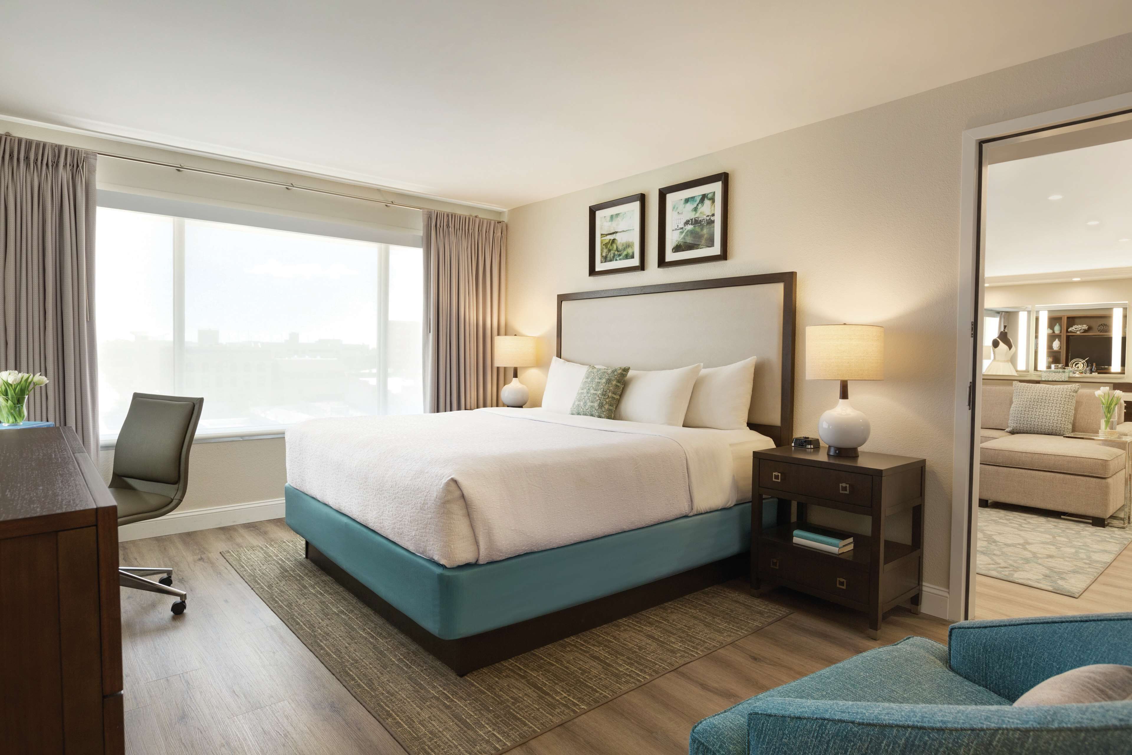 Quarto de hotel com cama grande, escrivaninha, cadeira e vista da cidade.