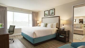 Habitación de hotel con cama, mesitas de noche, escritorio, silla, ventana grande y espejo.