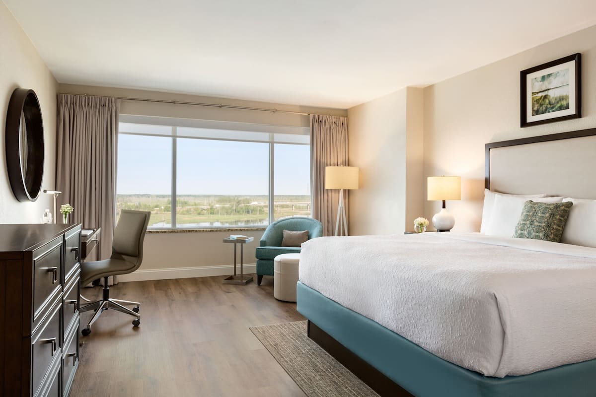 A hotel room with a large bed, a desk with a chair, a small table, and a view of the outdoors.