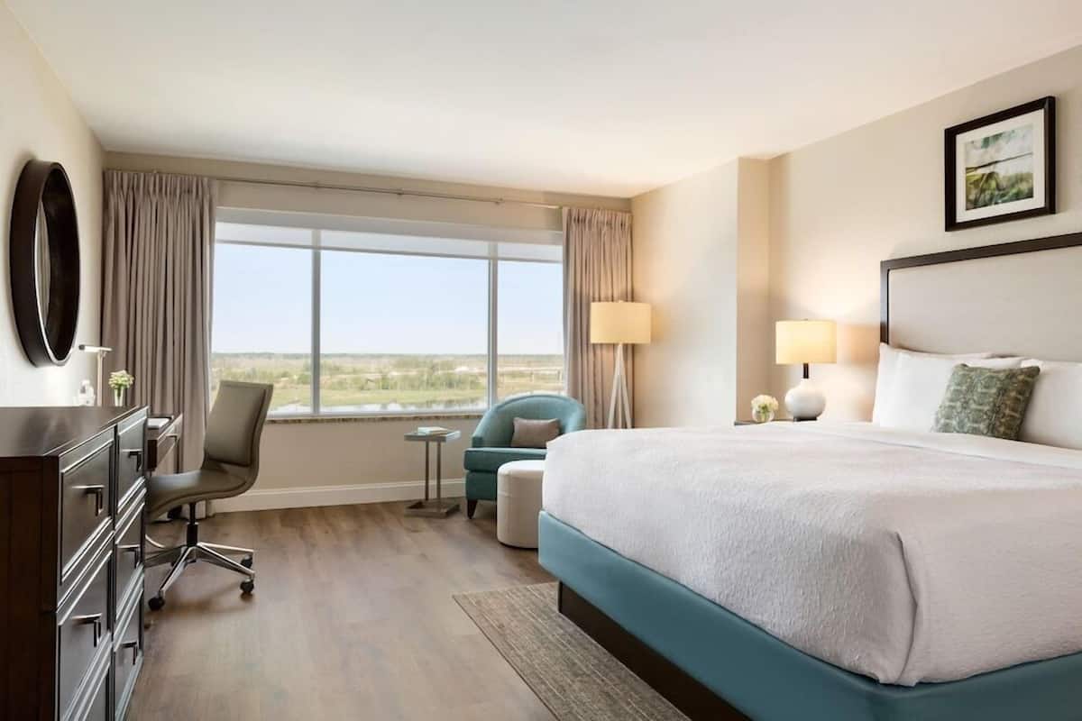 A hotel room with a large bed, a desk with a chair, a small table, and a view of the outdoors.