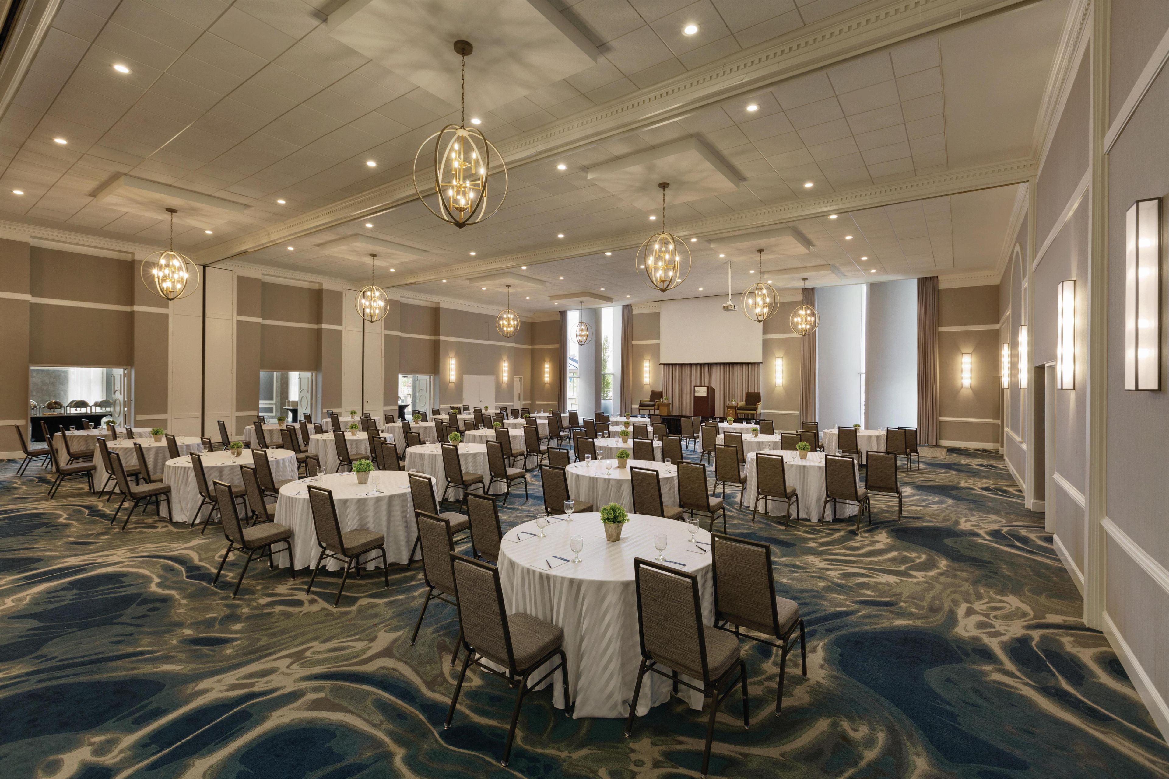 A large conference room with round tables and chairs, chandeliers, and a marble-patterned carpet.