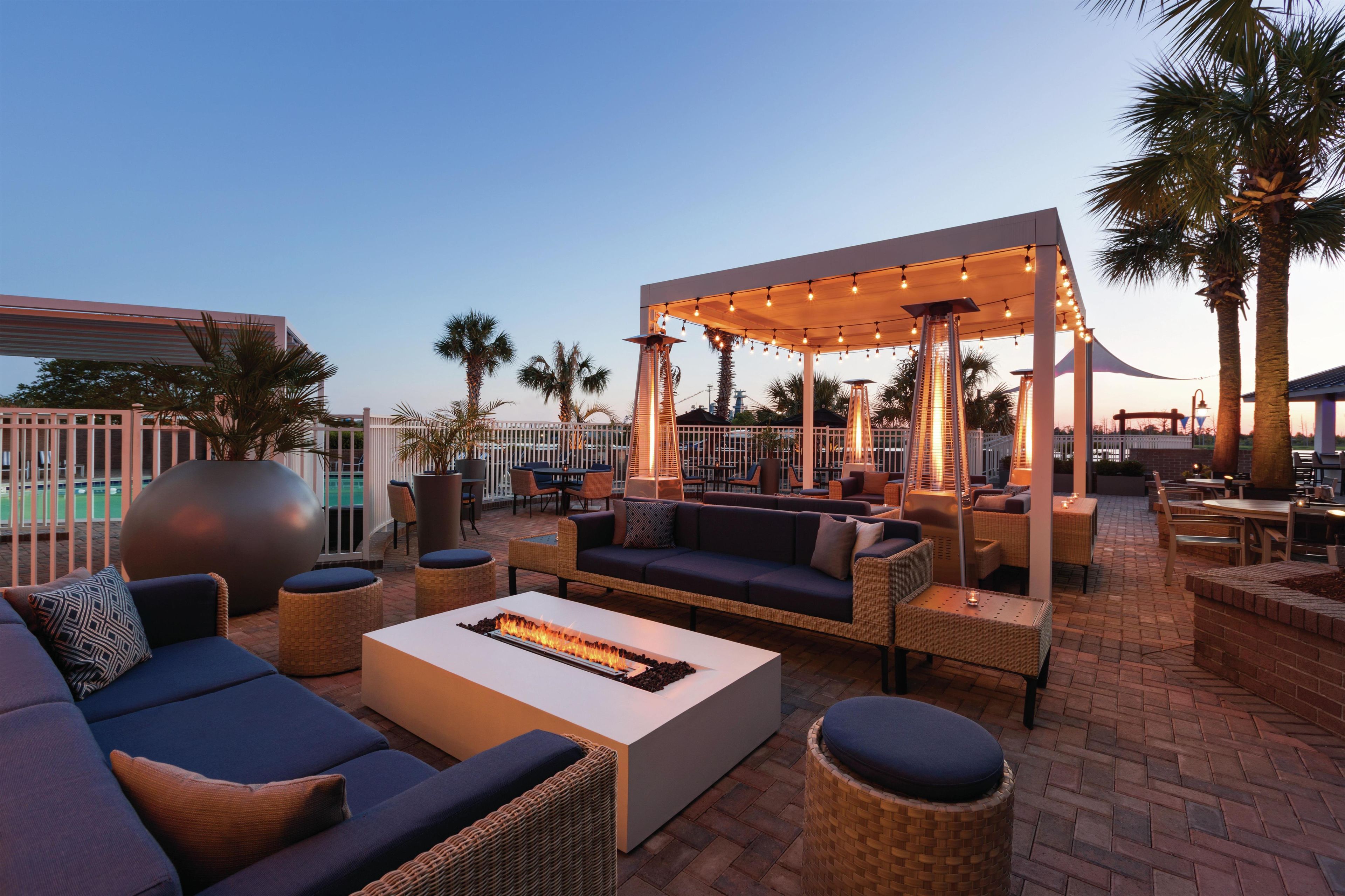 An outdoor seating area with sofas, a fire feature, and a covered section with string lights.