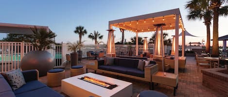 An outdoor seating area with sofas, a fire feature, and a covered section with string lights.