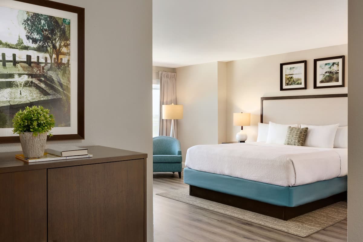 A hotel room with a bed, bedside table, lamp, and a framed picture on the wall.