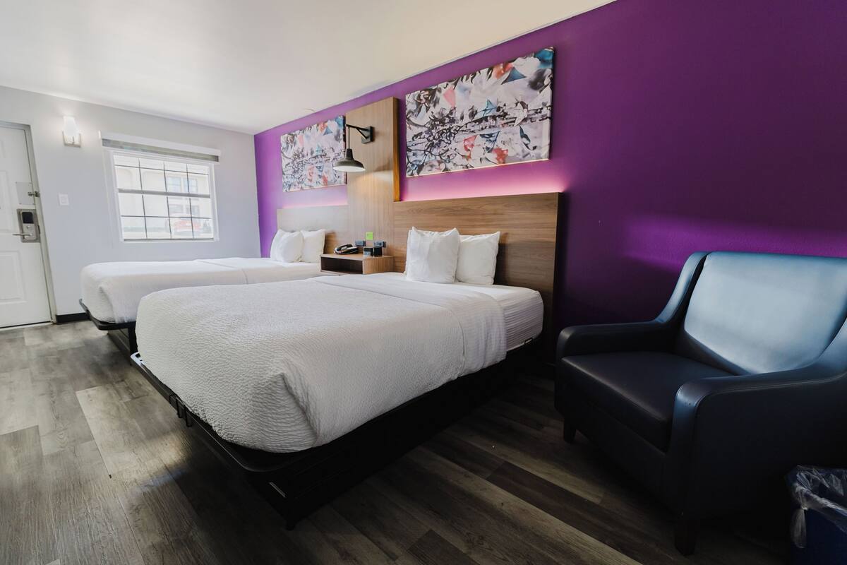 A hotel room with two beds, a desk, and a chair.
