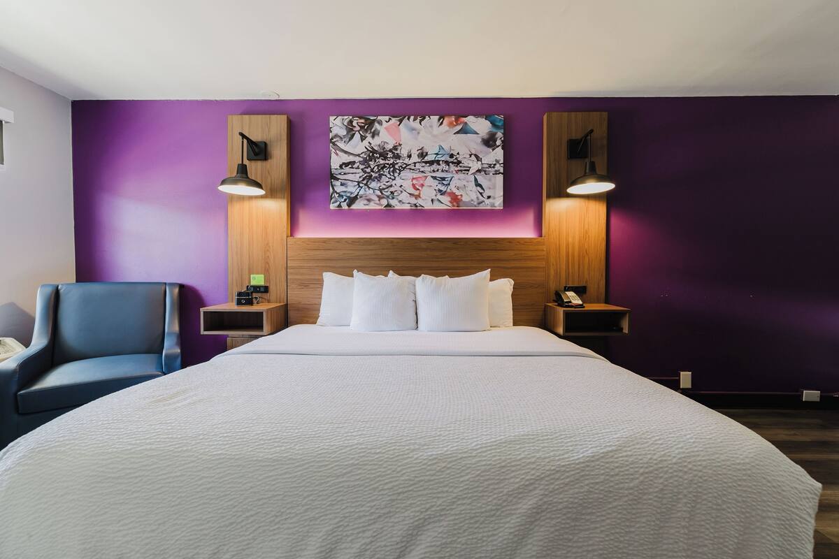 A modern hotel room with a large bed, purple walls, and two bedside tables with lamps.
