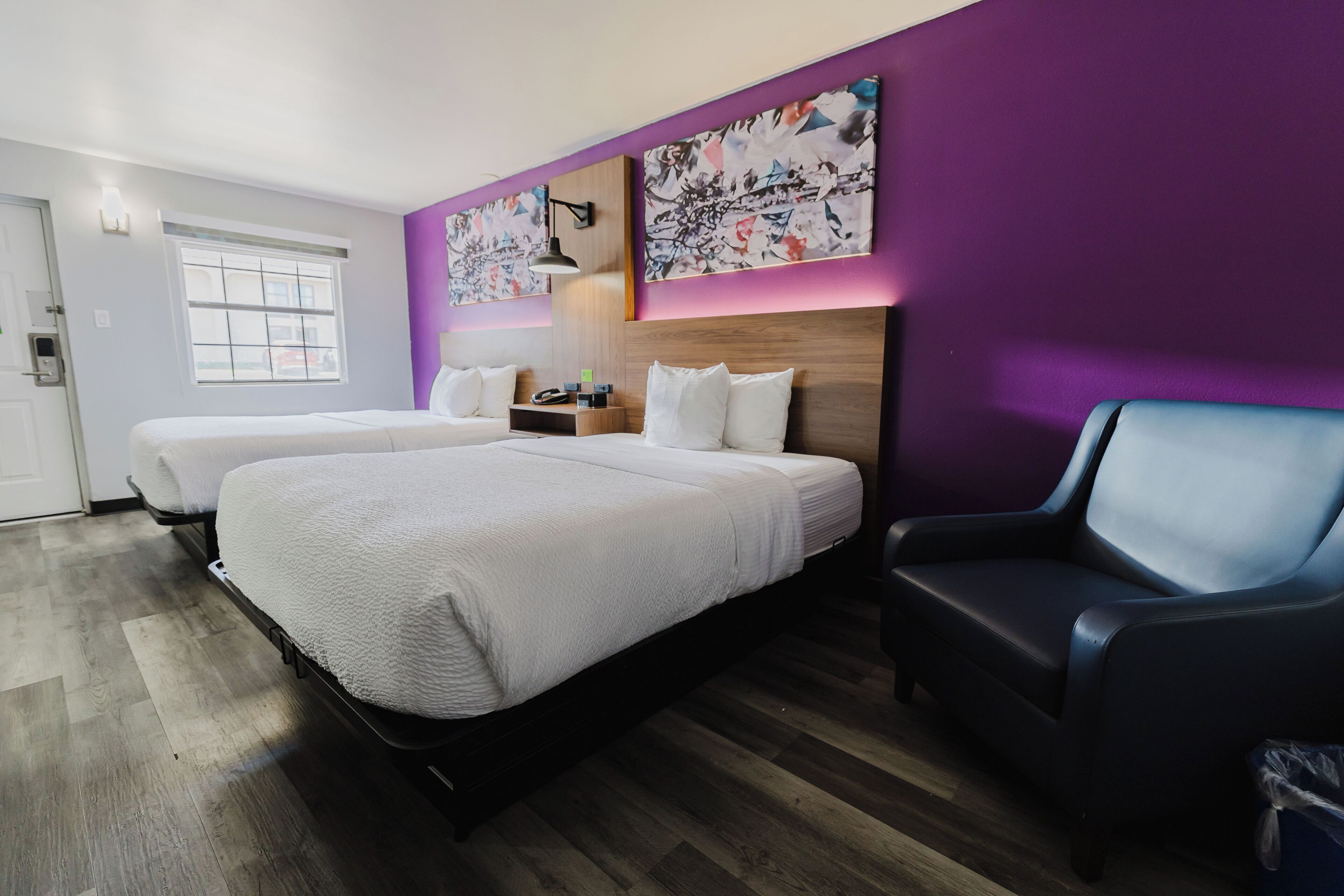 A hotel room with two beds, a desk, a chair, and artwork on the walls.