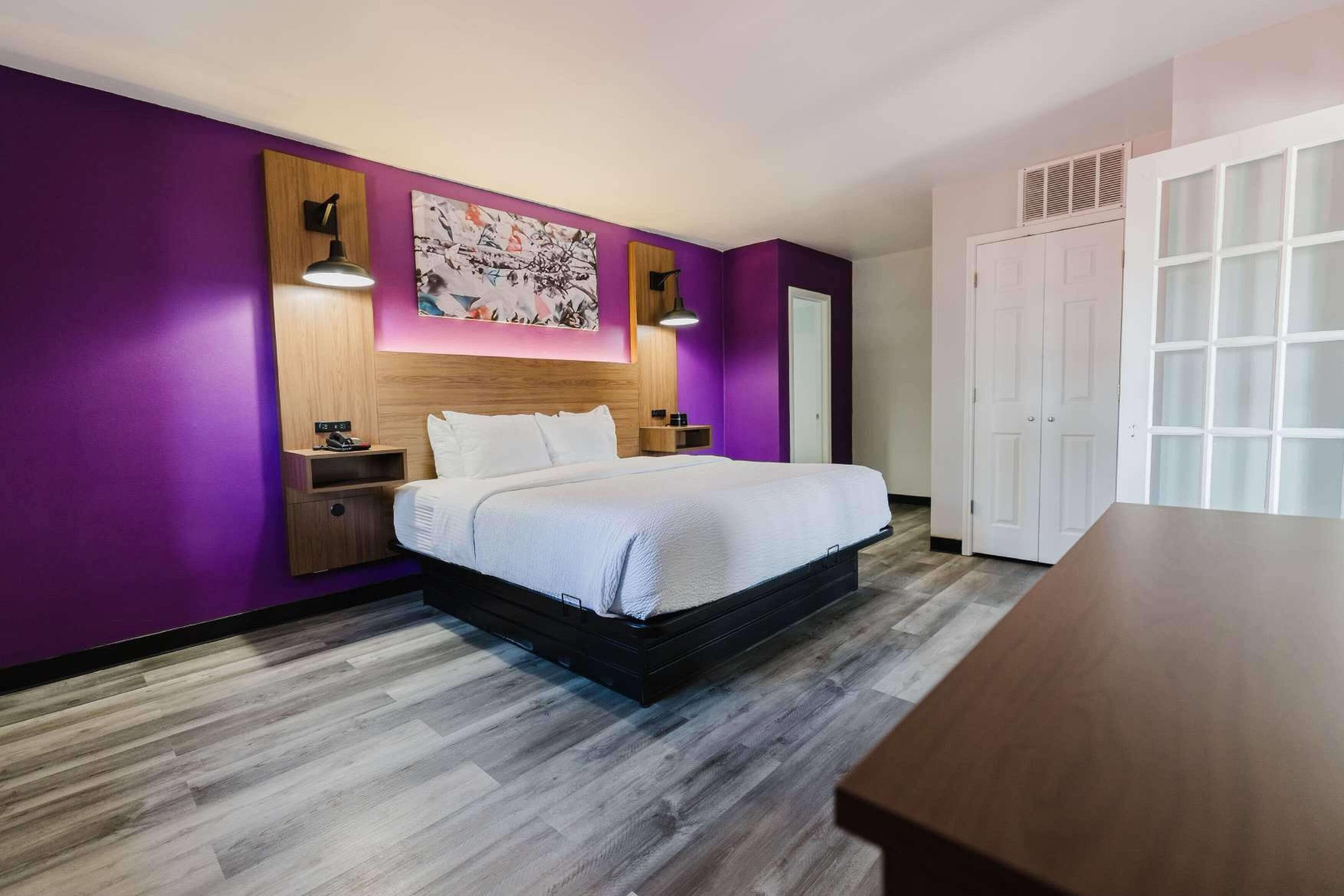 Un dormitorio moderno con una cama grande, paredes moradas y un cabecero de madera.