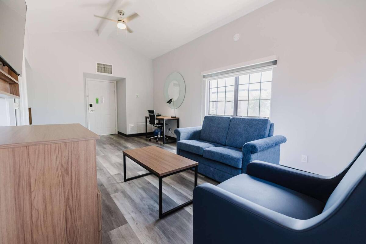 A modern living room with a blue sofa, a wooden coffee table, and a desk with a chair.
