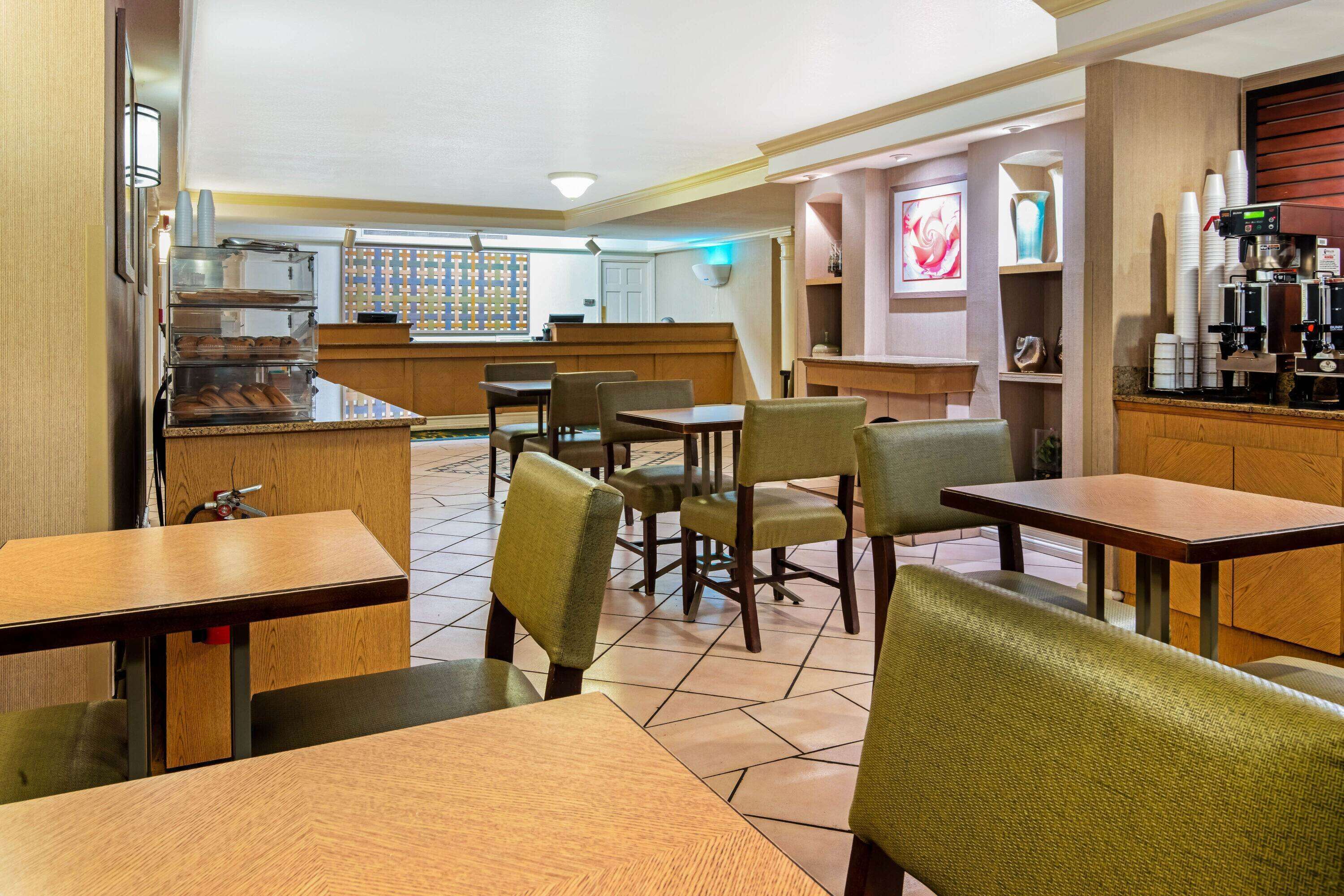 Un restaurante con mesas y sillas de madera, una barra con una máquina de café y una pared decorativa.