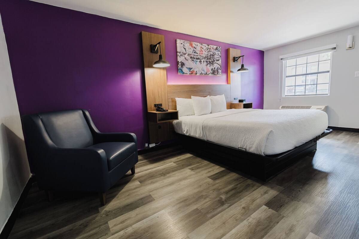 A modern hotel room with a large bed, a desk, a chair, and a window.