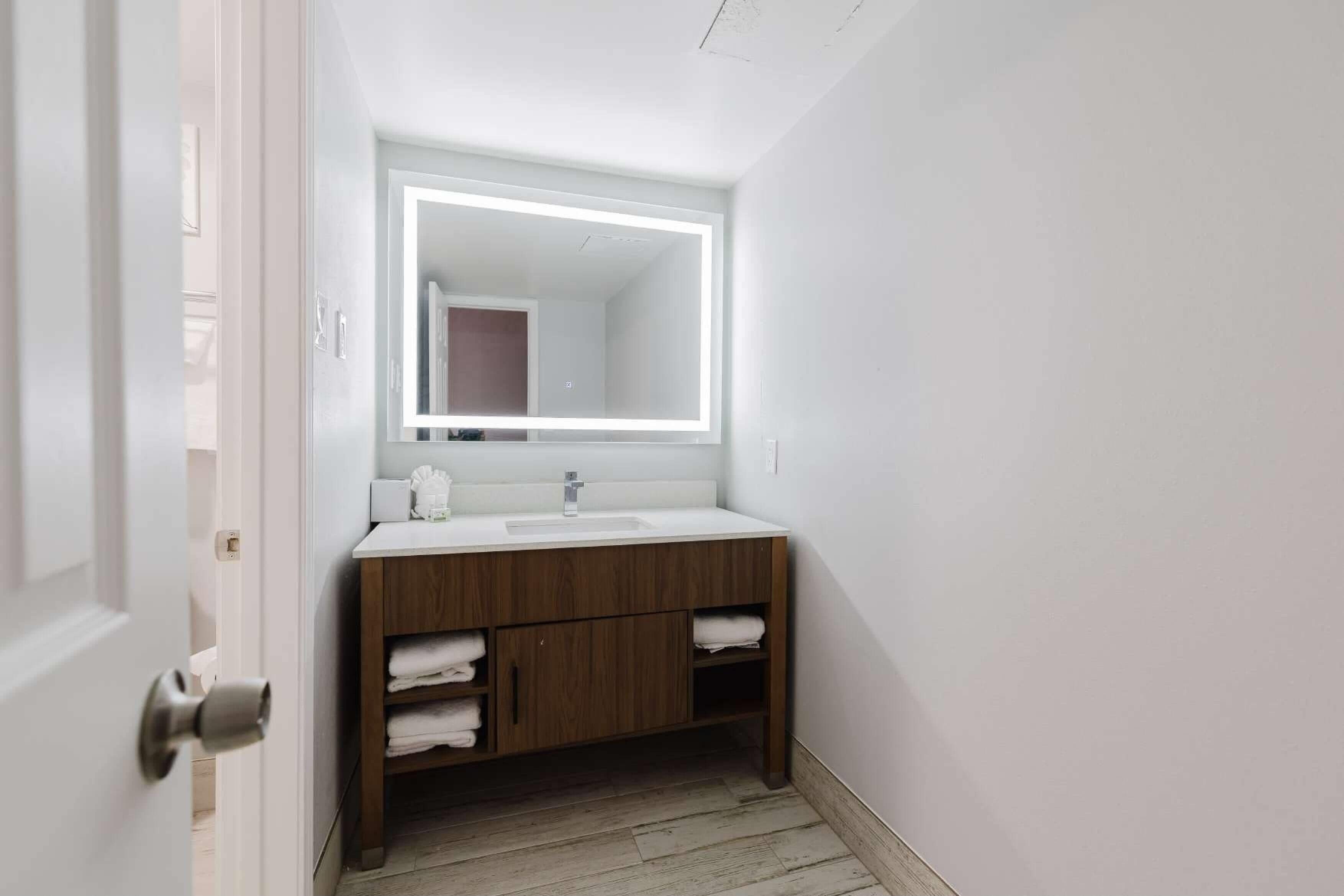 Ein modernes Badezimmer mit einem weißen Waschtisch, einem großen Spiegel und Holzschränken.