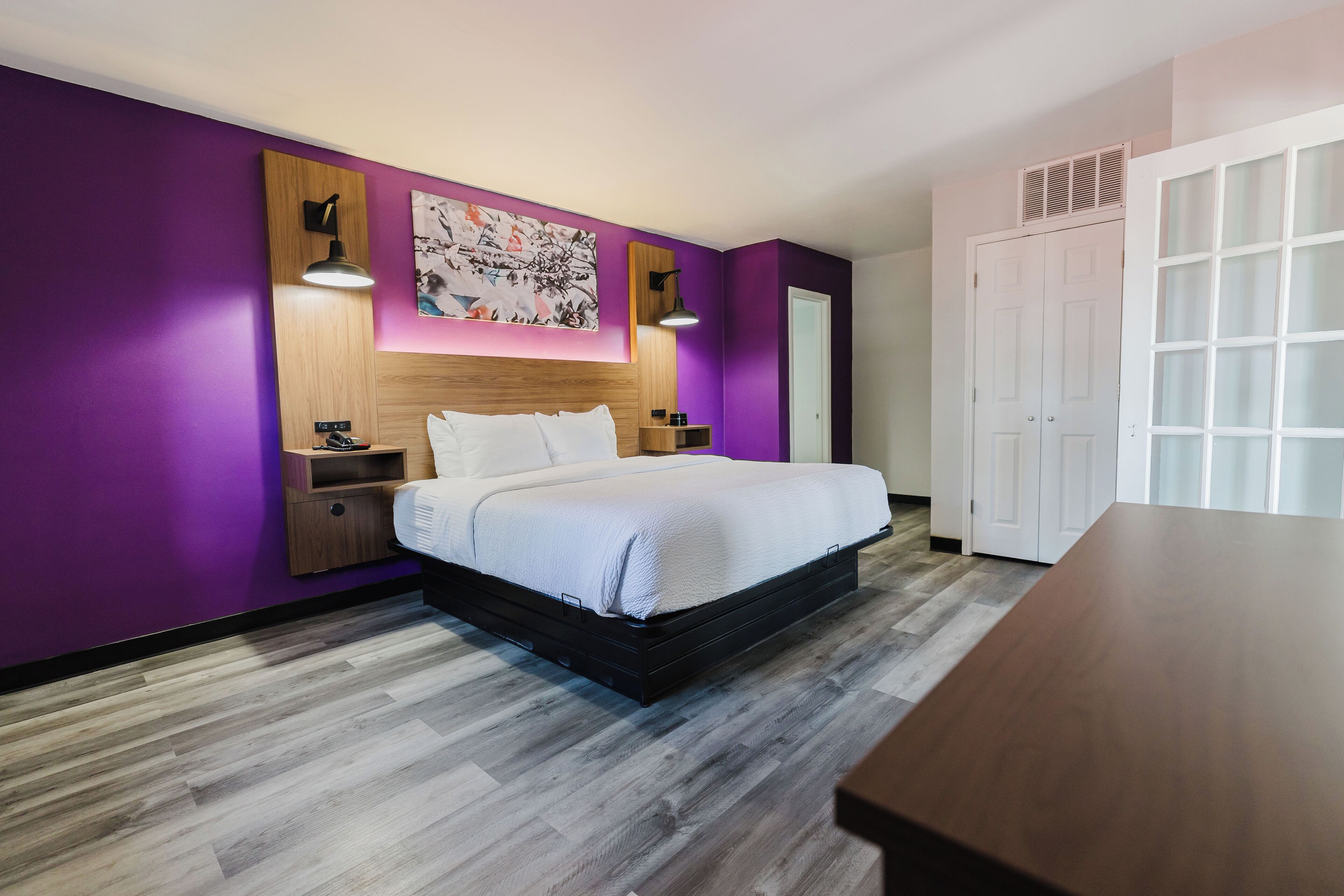 A modern bedroom with a bed, purple walls, a wooden headboard, and a white door.