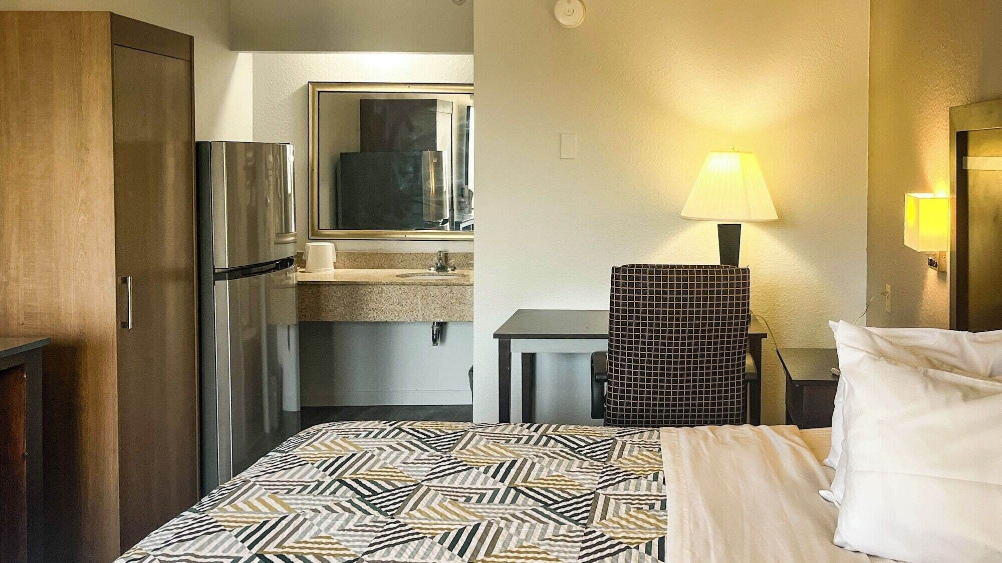 Une chambre d’hôtel équipée d’un lit, d’un bureau, d’une chaise, d’un réfrigérateur, d’un lavabo et d’un miroir.
