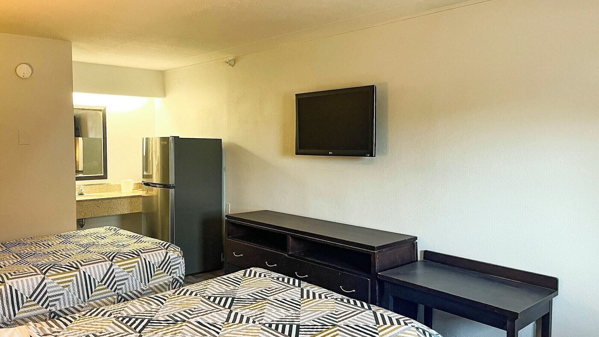 A hotel room with two beds, a refrigerator, a small table, and a wall-mounted TV.