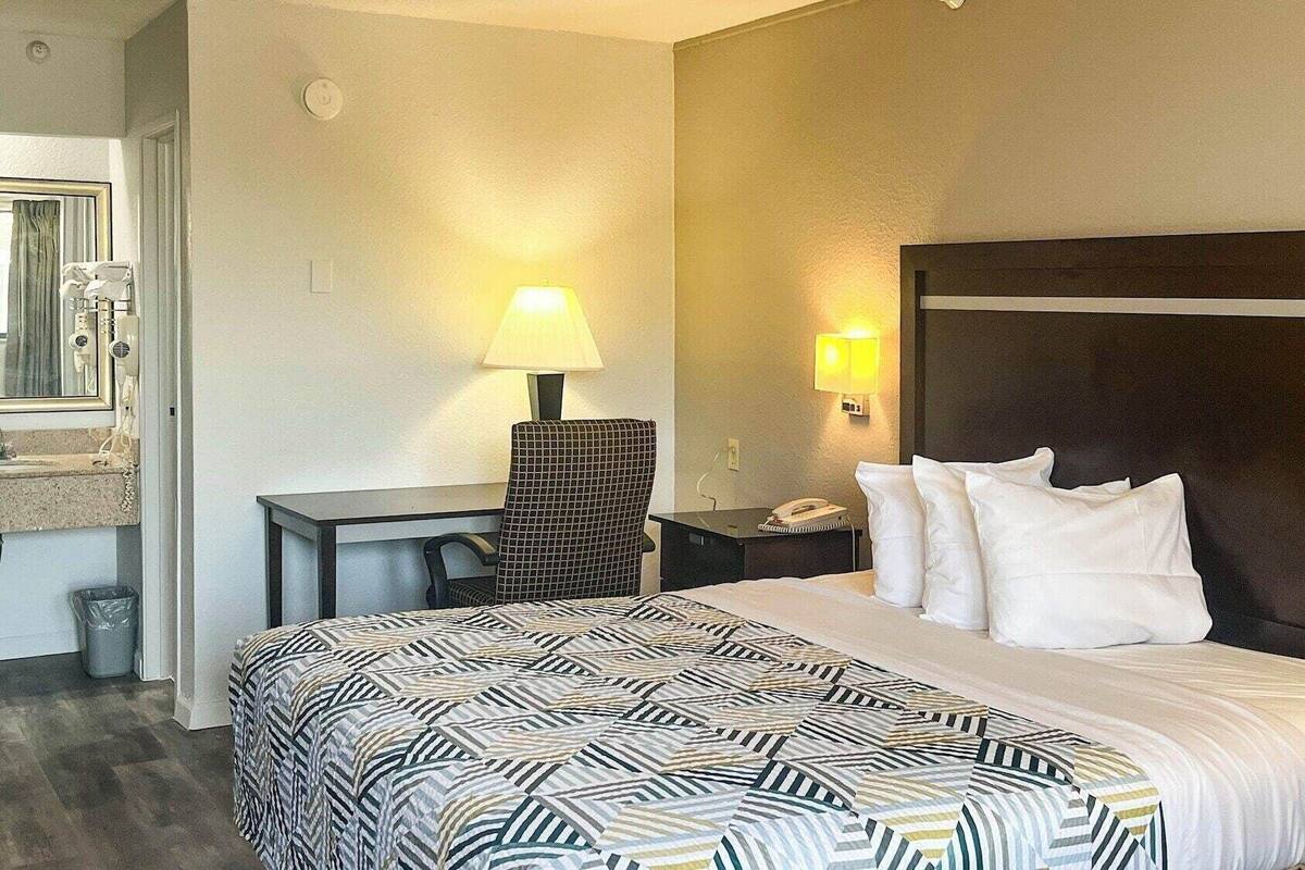 A hotel room with a bed, a desk, a chair, a lamp, and a nightstand.