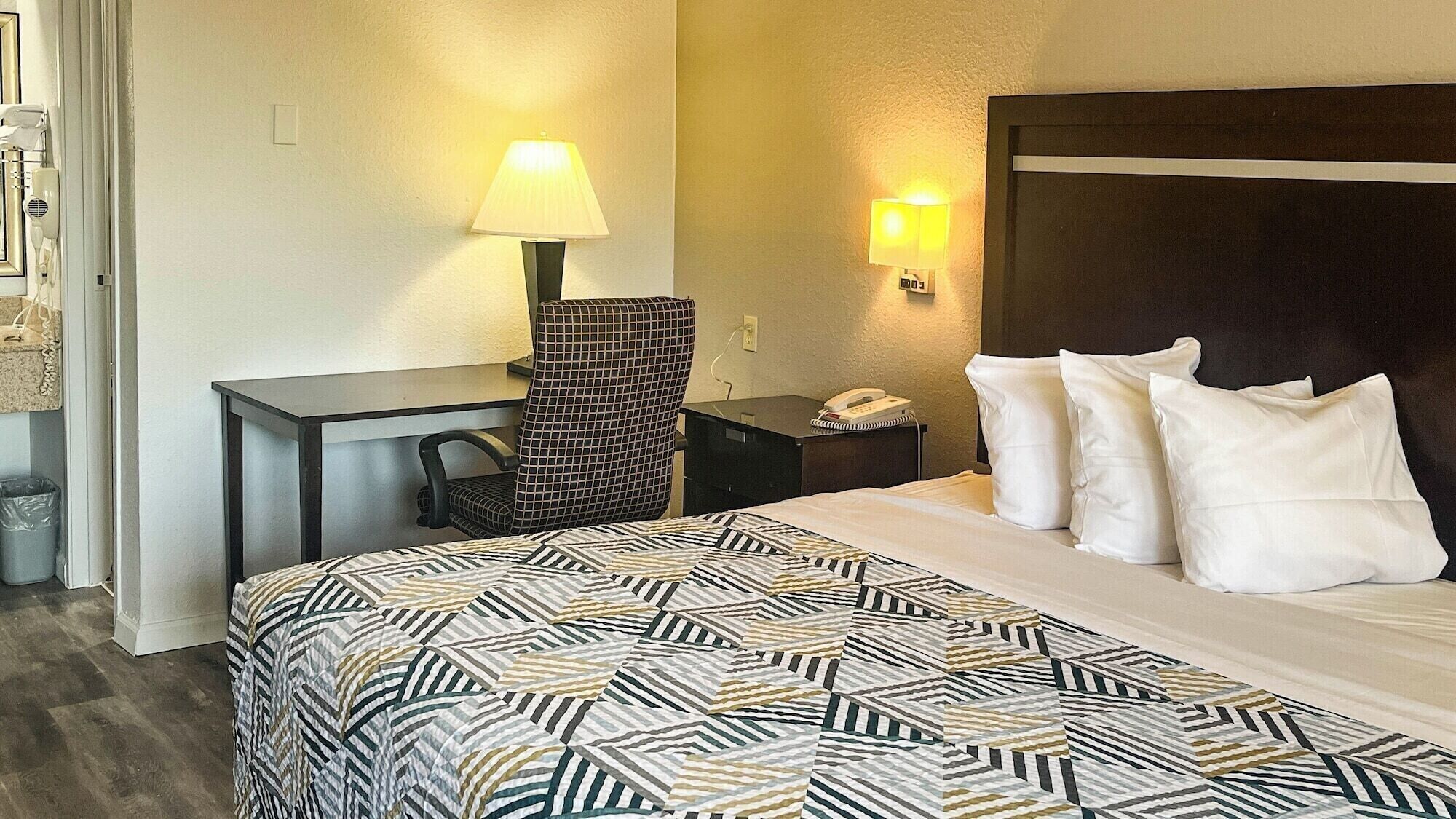 A hotel room with a bed, a desk, a chair, a lamp, and a telephone.