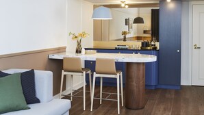 A modern kitchen with a marble countertop, two bar stools, a large mirror, and a pendant light.