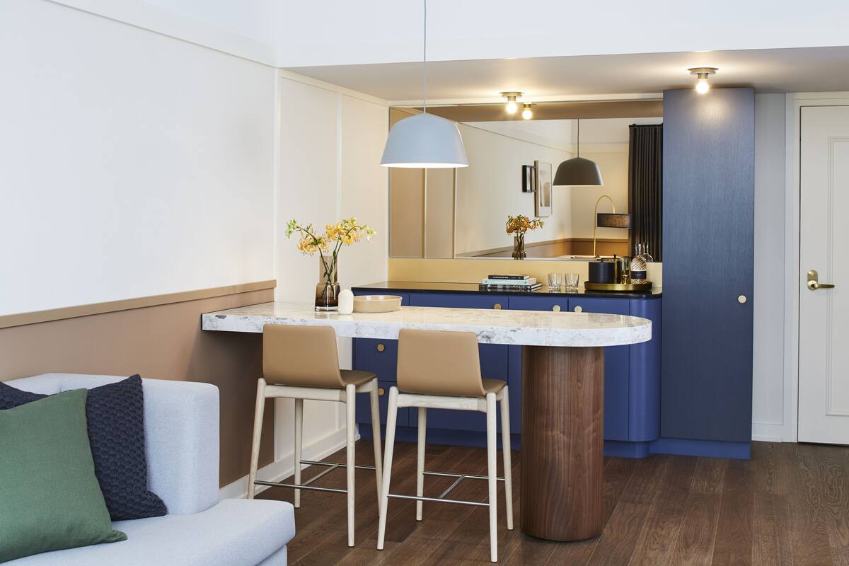 A modern kitchen with a marble countertop, two bar stools, a large mirror, and a pendant light.