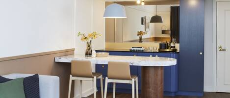 A modern kitchen with a marble countertop, two bar stools, a large mirror, and a pendant light.
