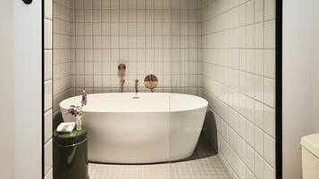 A modern bathroom with a freestanding bathtub, a toilet, and a trash can.