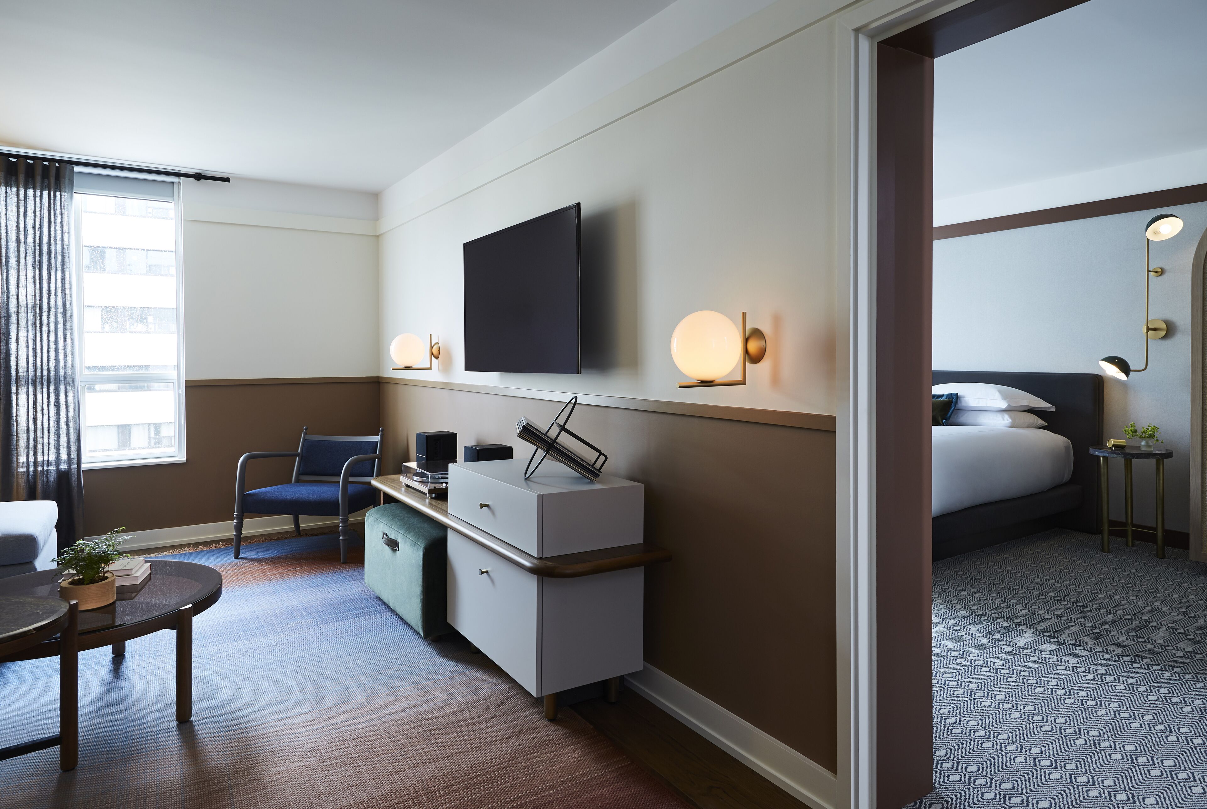 A hotel room with a flat-screen TV, bedside lamps, a desk with a chair, a bed, and a small table with a plant.