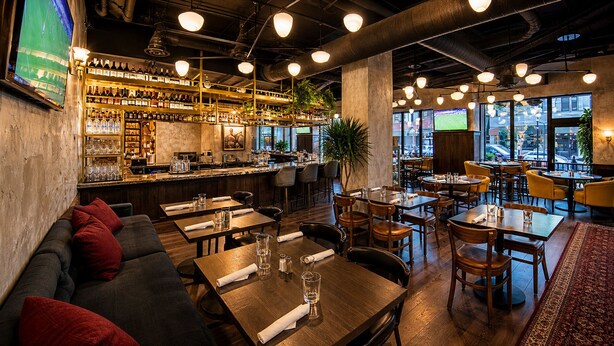 A bar area with shelves of bottles, a counter, and seating with tables and chairs. - Kimpton Saint George by IHG (Toronto)
