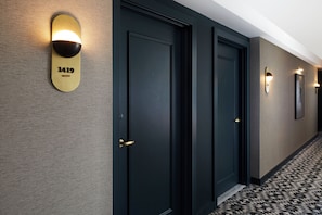 Un pasillo de hotel con tres puertas, cada una con una placa de número y apliques de luz en la pared.