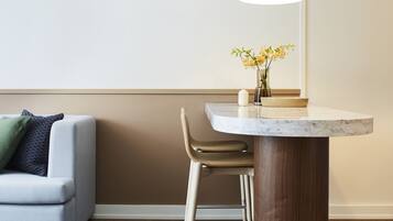 A modern dining area with a round marble table, a vase with yellow flowers, and a bar stool.