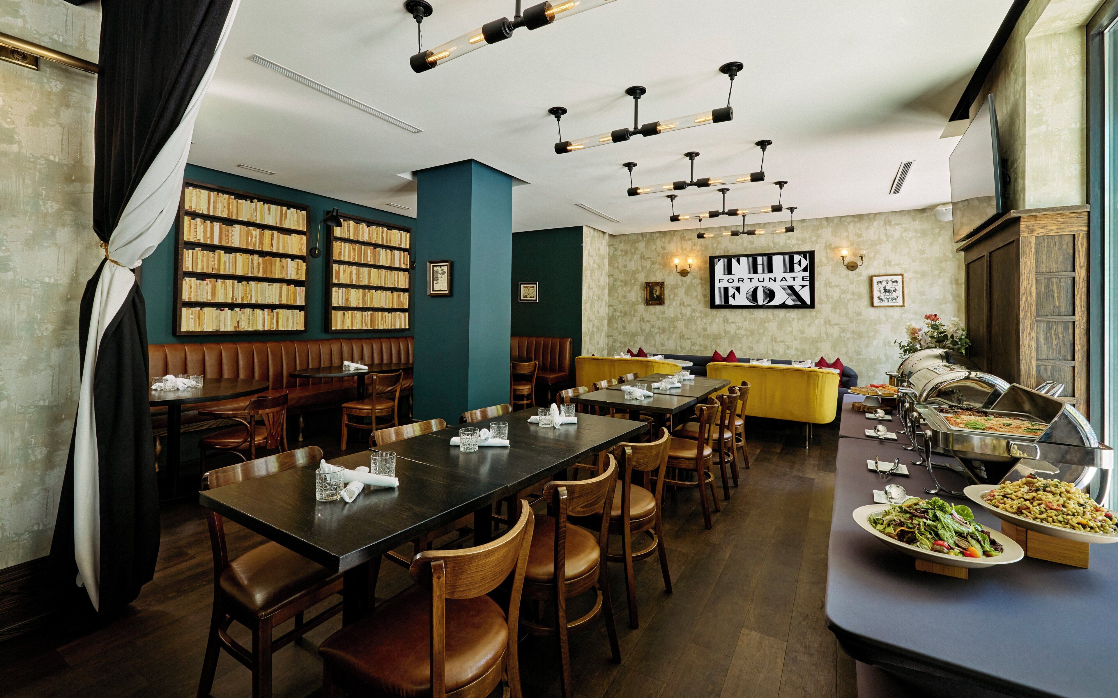 A restaurant with multiple dining tables, chairs, a buffet area, and bookshelves.