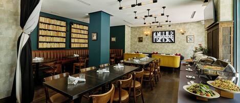 A restaurant with multiple dining tables, chairs, a buffet area, and bookshelves.