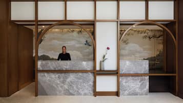 Bancada de recepção com tampo de mármore, ladeada por painéis de madeira e um mural com paisagem.