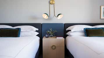 A hotel room with two beds, a nightstand with a clock and a vase, and a wall-mounted light fixture.