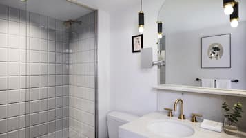 A modern bathroom with a white tiled shower, a sink with gold fixtures, and a large mirror with wall-mounted lights.