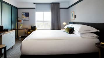 Una habitación de hotel con una cama grande, un escritorio, una silla, una lámpara y una ventana con cortinas.