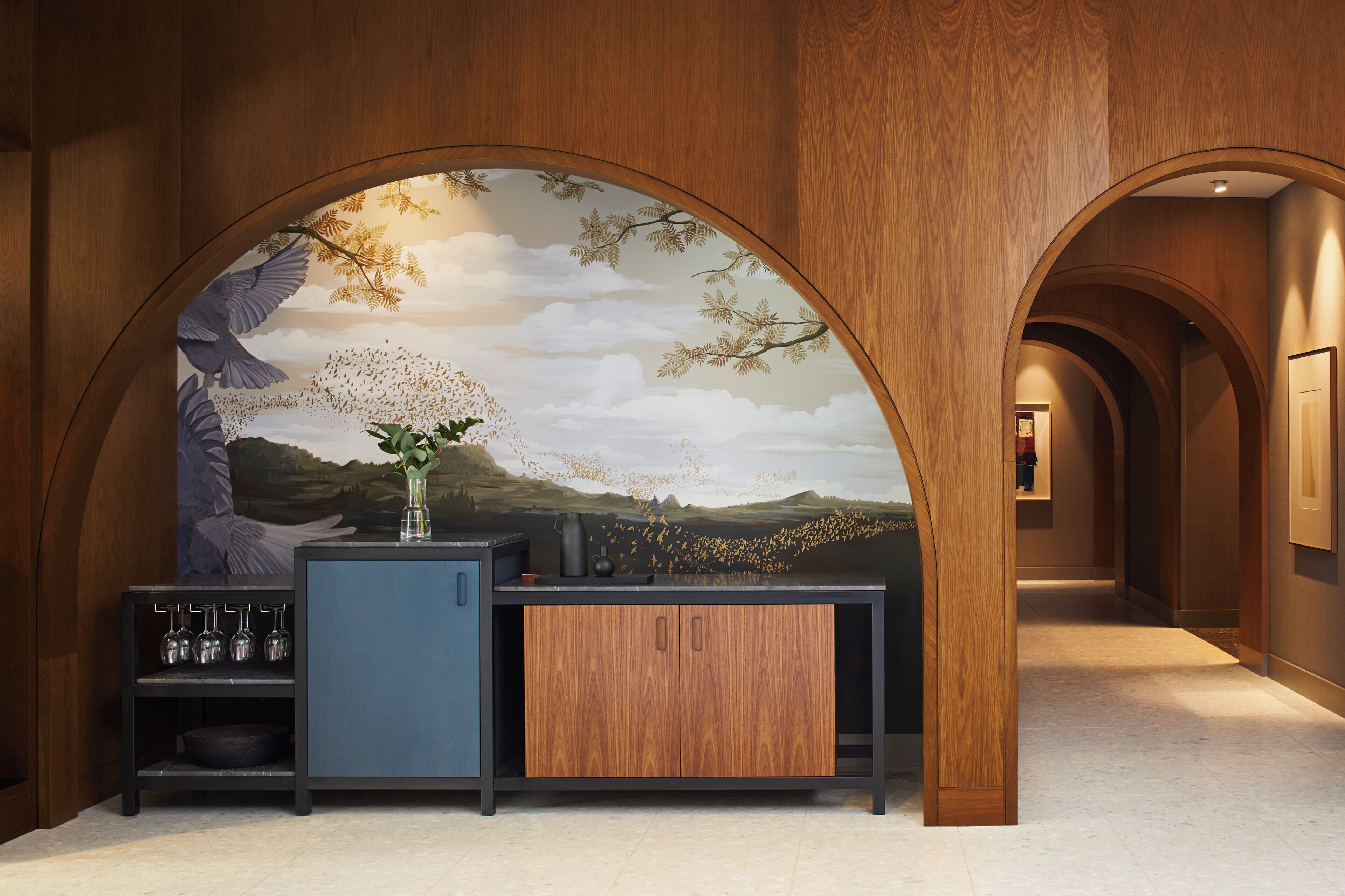 A modern interior with a wooden archway, a mural of a landscape, and a bar area with a cabinet and a vase.