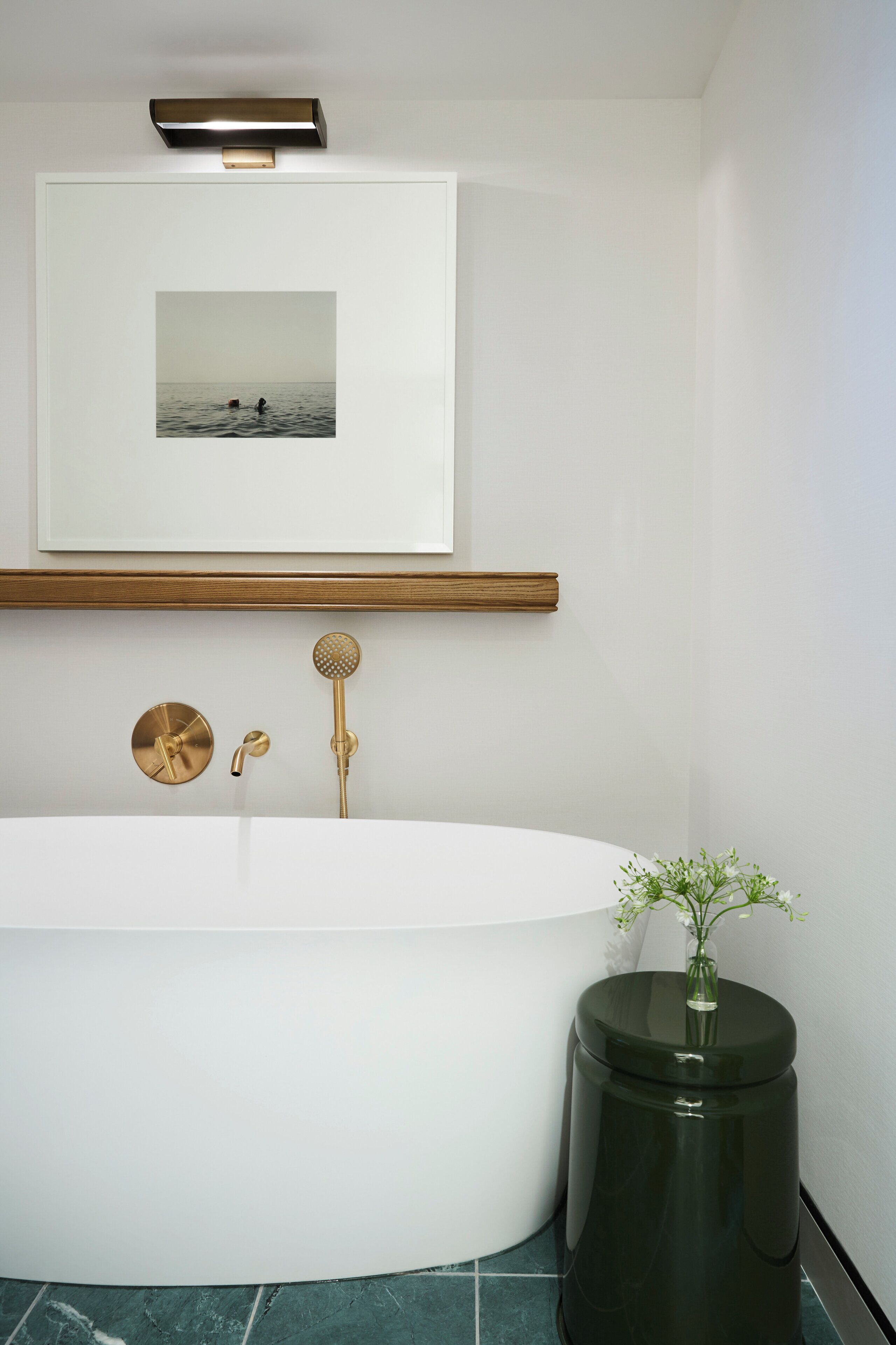 Un baño moderno con una bañera independiente, un cuadro enmarcado encima y una pequeña mesa redonda con un jarrón de flores.