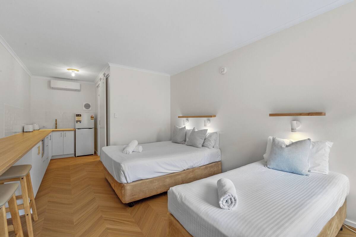 Ett hotellrum med två sängar, ett litet kök och ett trägolv.