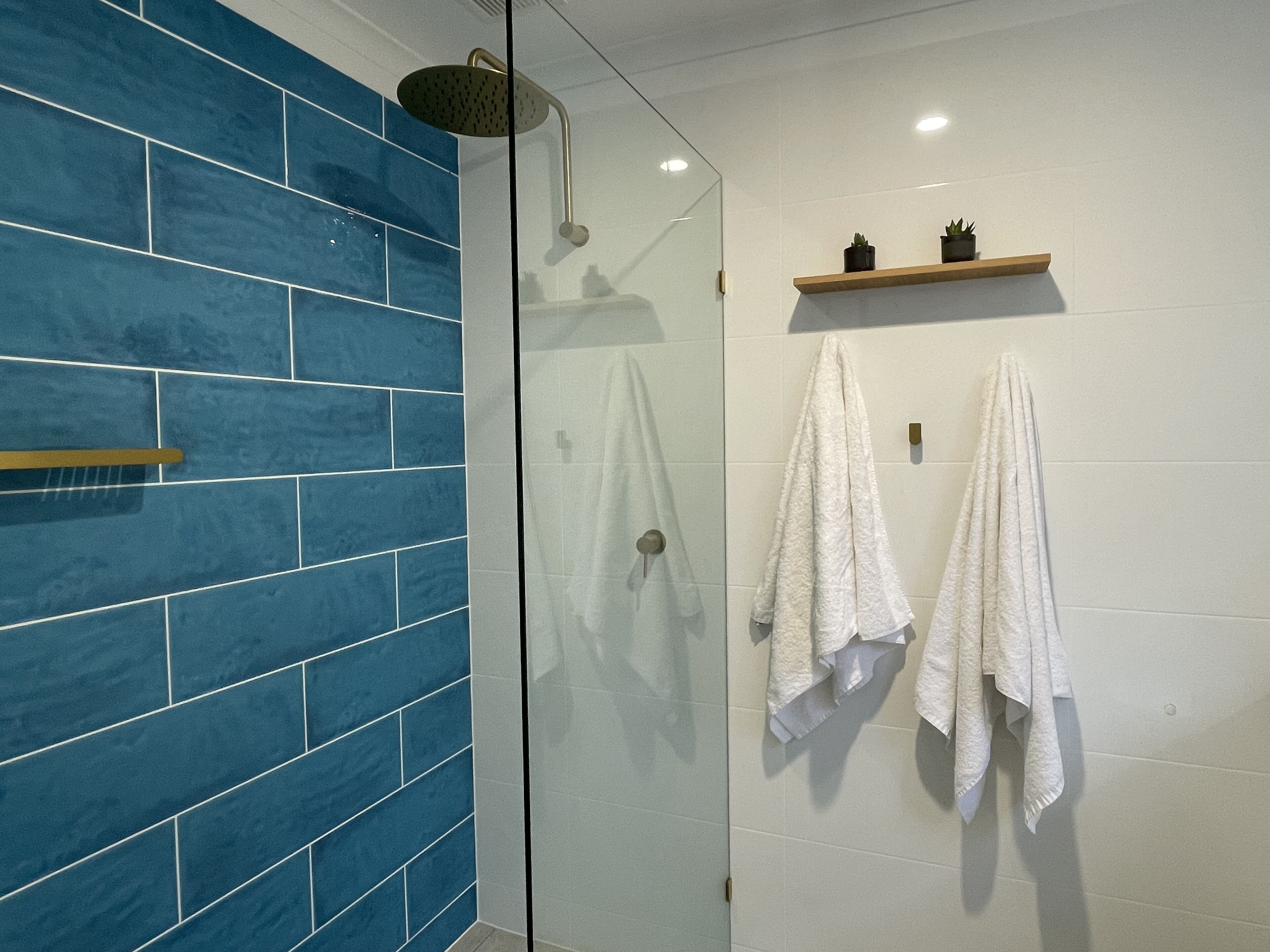 A bathroom with blue tiles, a glass shower enclosure, and two white towels hanging on the wall.