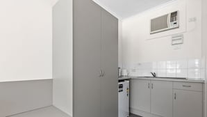 A compact kitchen with grey cabinets, a built-in dishwasher, and a wall-mounted air conditioning unit. - Taft Motor Inn (Glenelg)