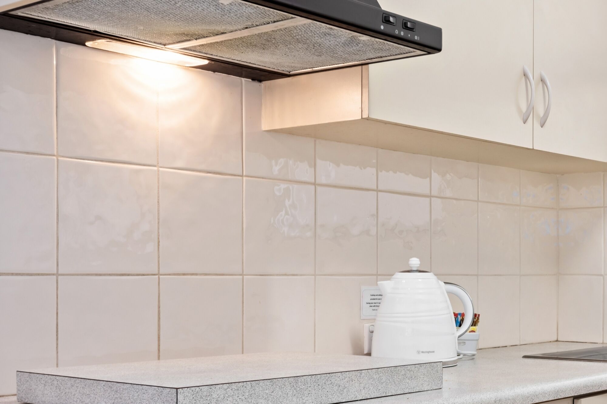 Una cocina con azulejos blancos, estufa integrada y una cafetera sobre la encimera.